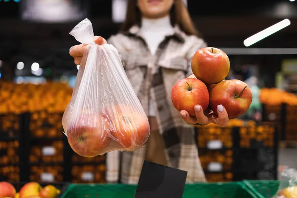 Woman is thinking whether to take apples in a plastic bag or do without. Girl buys fruit in a supermarket. Concept of a world without plastic
