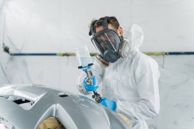 Otomobil boyacısı, boyama kabininde araba gövdesini cilalıyor. Tamirci, aracın vücut parçalarını onarır.