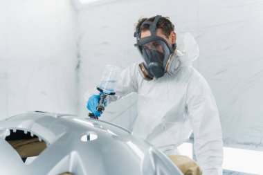 Otomobil boyacısı, boyama kabininde araba gövdesini cilalıyor. Tamirci, aracın vücut parçalarını onarır.