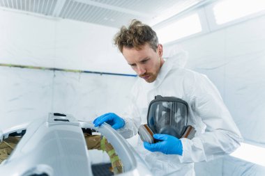 Bir resim kabininde çalışan genç bir araba boyacısı. Bir otomobil servisinde araç gövdesi onarımının süreci