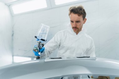 Genç kıvırcık araba boyacısı araba tamponunu cilalıyor. Adam sprey kabininde çalışıyor. Araba vücut parçalarının boyanması süreci