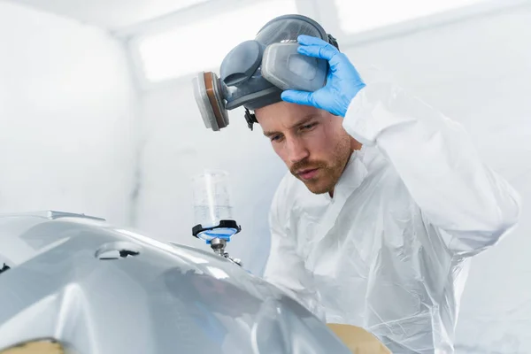 Young male car painter checks the quality of painting. Car service worker at work