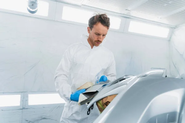 Car colorist man selecting color of automobile body element with paint matching samples