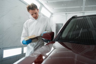 Boyama odasındaki oto boyacı örneklerle araba boyasının rengini seçer