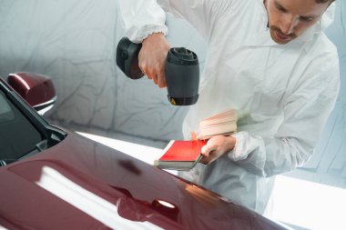 Araba boyacısı, özel bir boyacı lambası kullanarak bir aracın vücut renginin doğru tonunu belirler. Otomobil tamircisi garajda.