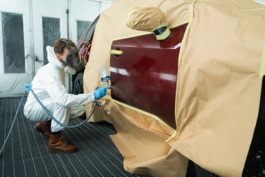 Koruyucu takım elbiseli bir oto boyacı ve maske sprey tabanca kullanarak arabanın kapısına yağ püskürtücü veya diğer temizleyicileri sıkar. Yerel onarım için araç gövdesi elementlerinin hazırlanması