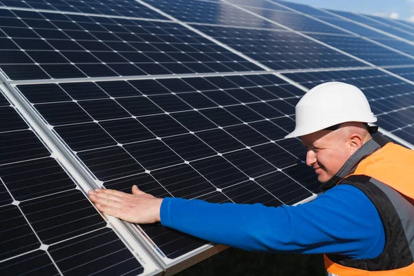 ハード帽子の太陽光発電所の労働者は 損傷のために彼の手で太陽光パネルの表面をチェックします — ストック写真