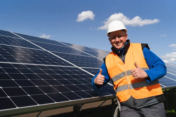 Elektrik santralinde güneş panellerinin yanında dururken başparmak hareketi gösteren tatmin olmuş işçi