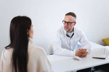 Beyaz labradorlu erkek doktor ofisinde kadın hastayla konuşuyor. Özel klinikteki randevu sırasında doktorla tedaviyi tartışan kadın