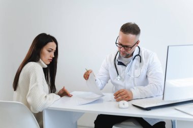 Erkek doktor, kadın hasta randevusu sırasında tıbbi belgeleri doldurur.