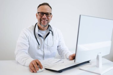 Bilgisayarın ofisinde çalışan gözlüklü orta yaşlı bir erkek doktorun portresi.