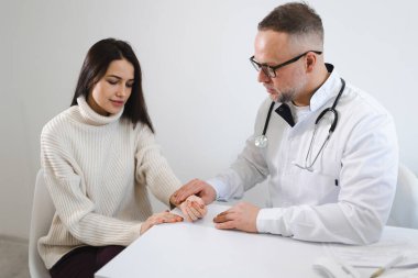 Erkek doktor klinikteki genç kadın hastanın nabzını ölçüyor. Hastanede muayene edilen bir kadın. Kalp atışlarını kontrol eden terapist.