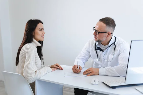 男性医師は患者のために処方箋を書いている 若い女性に相談する医師 — ストック写真
