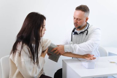 Erkek doktor, kadın hastanın koluna kan basıncı monitörünü takıyor.