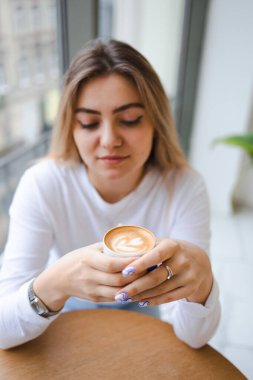 Kafkasyalı genç bir kadın kahve dükkanında otururken elinde bir kupa güzel kokulu kahve tutuyor.
