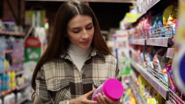 Marketin ev yapımı kimyasalları bölümünde çamaşır tozu paketinin etiketini okuyan kadın.