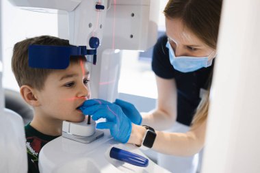 Kadın dişçi, panoramik diş radyografisini küçük bir çocuğa modern x-ray cihazı kullanarak götürüyor.