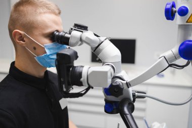 Diş tedavisi için mikroskop kullanan erkek dişçi.