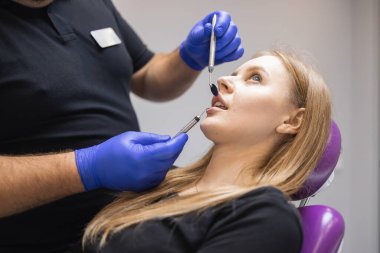 Erkek dişçi klinikte kadın hastanın dişlerini muayene ediyor.