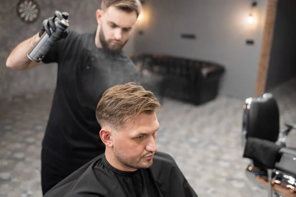 ヘアスプレーを使用して男にヘアスタイリングを行う男性理髪師 — ストック写真