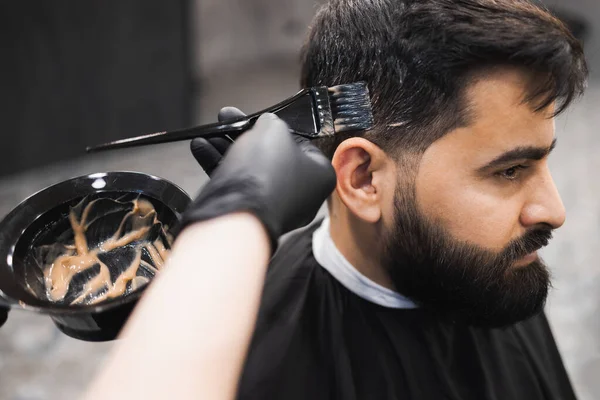 理容室で男性の依頼人の髪を死ぬプロの理容師 美容師はブラシでクライアントの髪に染料を適用します — ストック写真