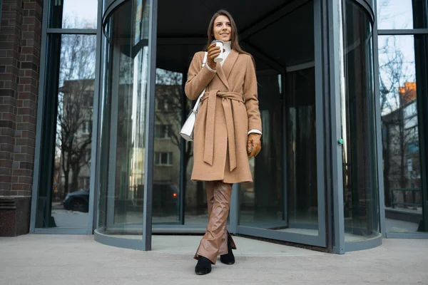 Szczęśliwa Kobieta Stylowych Ubraniach Filiżanką Kawy Pobliżu Wejścia Budynku Biurowego — Zdjęcie stockowe