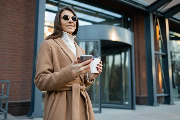 Kahverengi Ceketli Gözlüklü Elinde Bir Fincan Kahve Akıllı Bir Telefonla — Stok fotoğraf