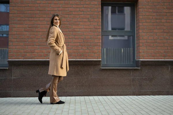 レンガの壁を持つ建物の近くにスタイリッシュな服を着た若い女性 — ストック写真