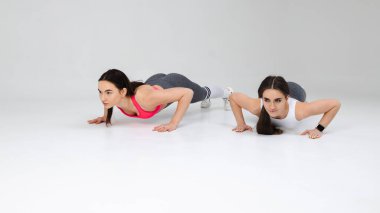 Stüdyoda yerden şınav çeken iki atletik kız.