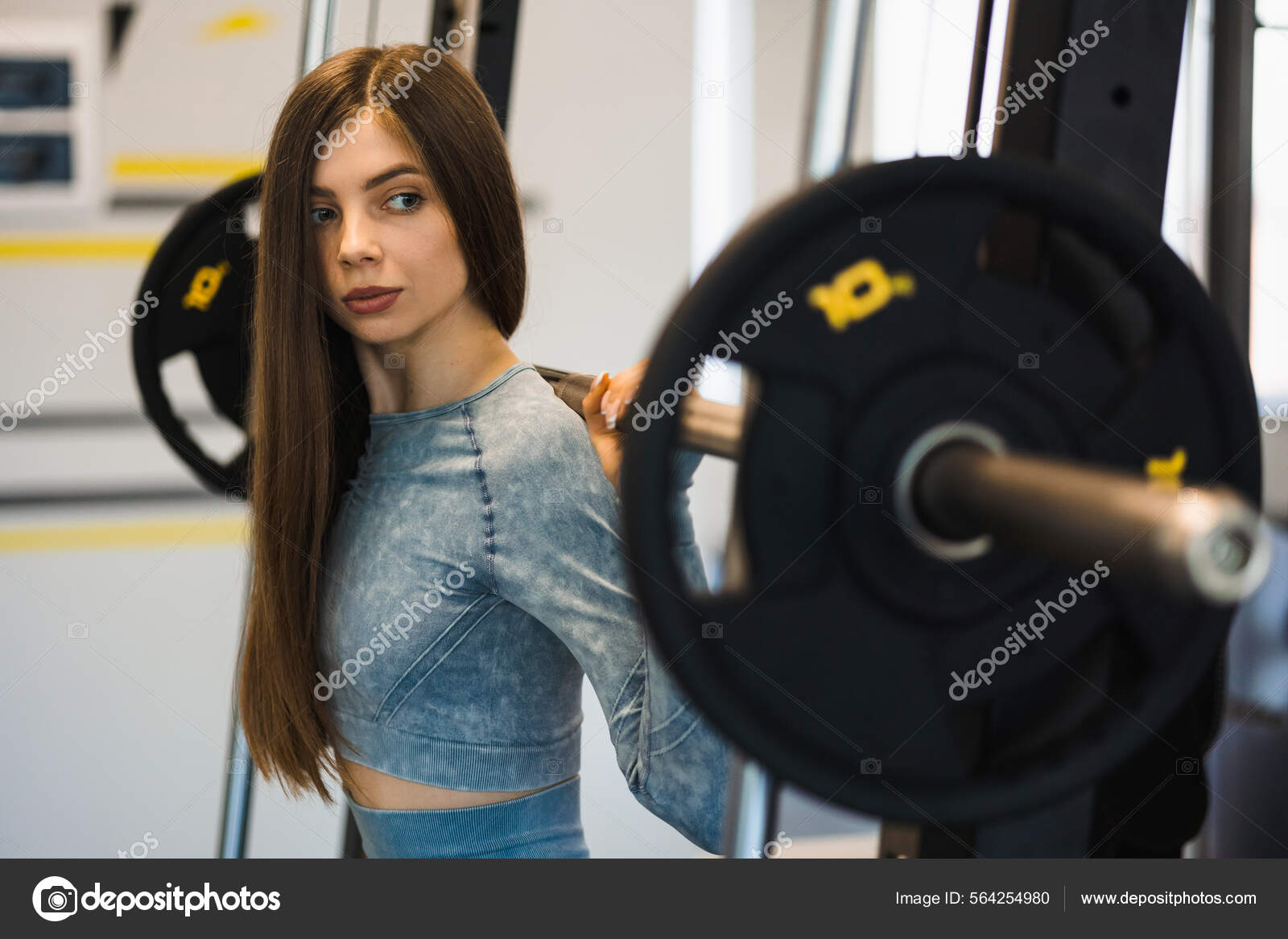 Chica fitness haciendo sentadillas con la barra en la máquina