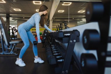 Spor salonunda dambıllarla egzersiz yapan atletik kız.