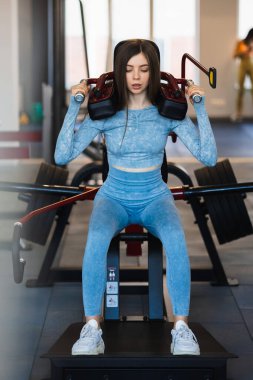 Genç, formda bir kadın egzersiz makinesinde çömeliyor.