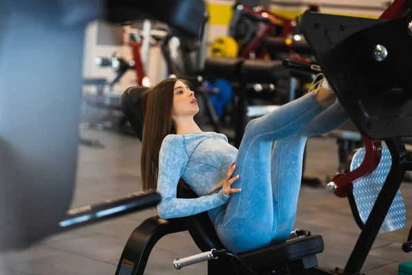 ジムで足のプレス機で運動をする青いスポーツウェアのアスリート女性 — ストック写真