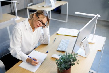 İş yerinde otururken deftere yazı yazan yorgun kadın ofis çalışanı.