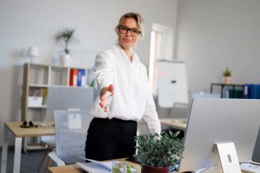 Olgun, hoş bir kadın selamlaşma partneri için elini uzatır. Dost canlısı bayan ofis çalışanı
