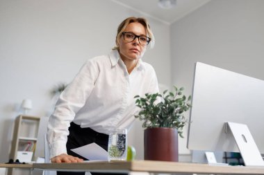 Ofisteki orta yaşlı, tatminsiz iş kadını kameraya öfkeyle bakıyor.