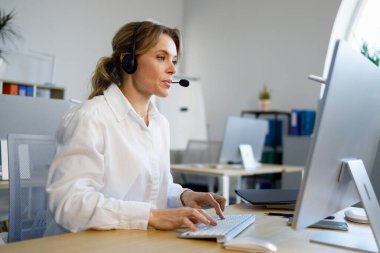 Ofisteki bilgisayarın başında mikrofon kulaklığı takan kadın çağrı merkezi operatörü oturuyor.