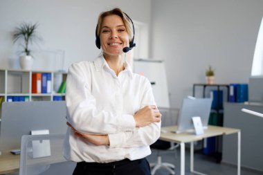 Gülümseyen kendine güvenen kadın destek operatörü ofiste kollarını kavuşturdu.