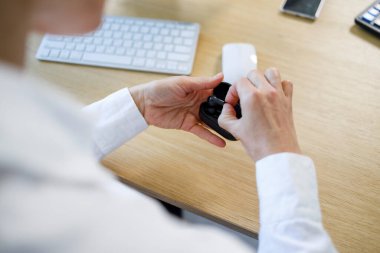Close-up of the hands of a business woman in a white shirt taking out wireless headphones from a case
