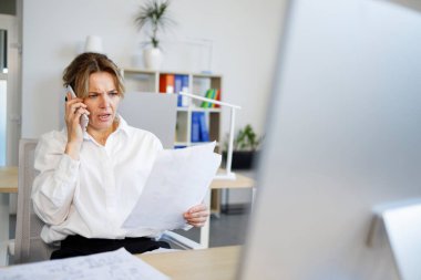 Belgelere bakarken telefonda konuşan şaşırmış yüzlü bir iş kadını.