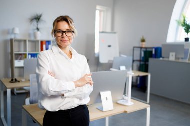 Ofiste kollarını kavuşturmuş kendinden emin bir iş kadınının portresi.