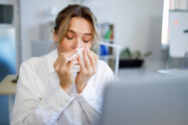 Olgun bir iş kadını ofisteki masasında oturup burnunu siliyor.