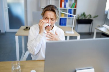 Upset businesswoman crying into handkerchief while sitting at workplace in office