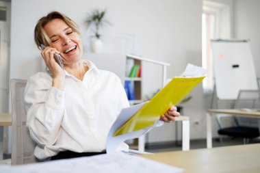 Ofiste otururken cep telefonuyla konuşan gülen iş kadını.