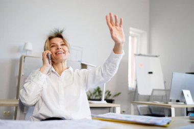 İş kadını telefonda konuşuyor ve meslektaşlarını selamlamak için el sallıyor.