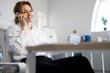 Ofiste akıllı telefondan konuşan olgun bir iş kadını.