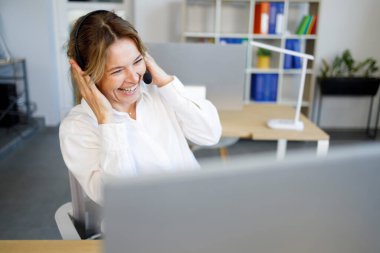 Kulaklık takmış bir ofis çalışanı video çağrısında gülüyor.