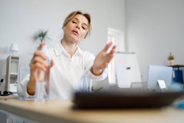 İş kadını ofis çalışanı ellerine antiseptik sürüyor.