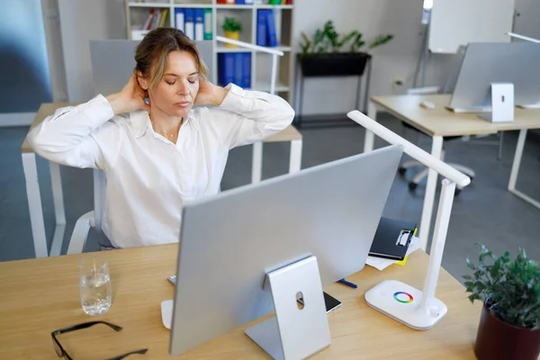 Female office worker stretching for relaxing while working at computer. Business woman massaging her neck while sitting at workplace