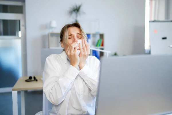 Sick businesswoman sneezing in a tissue while working in the office